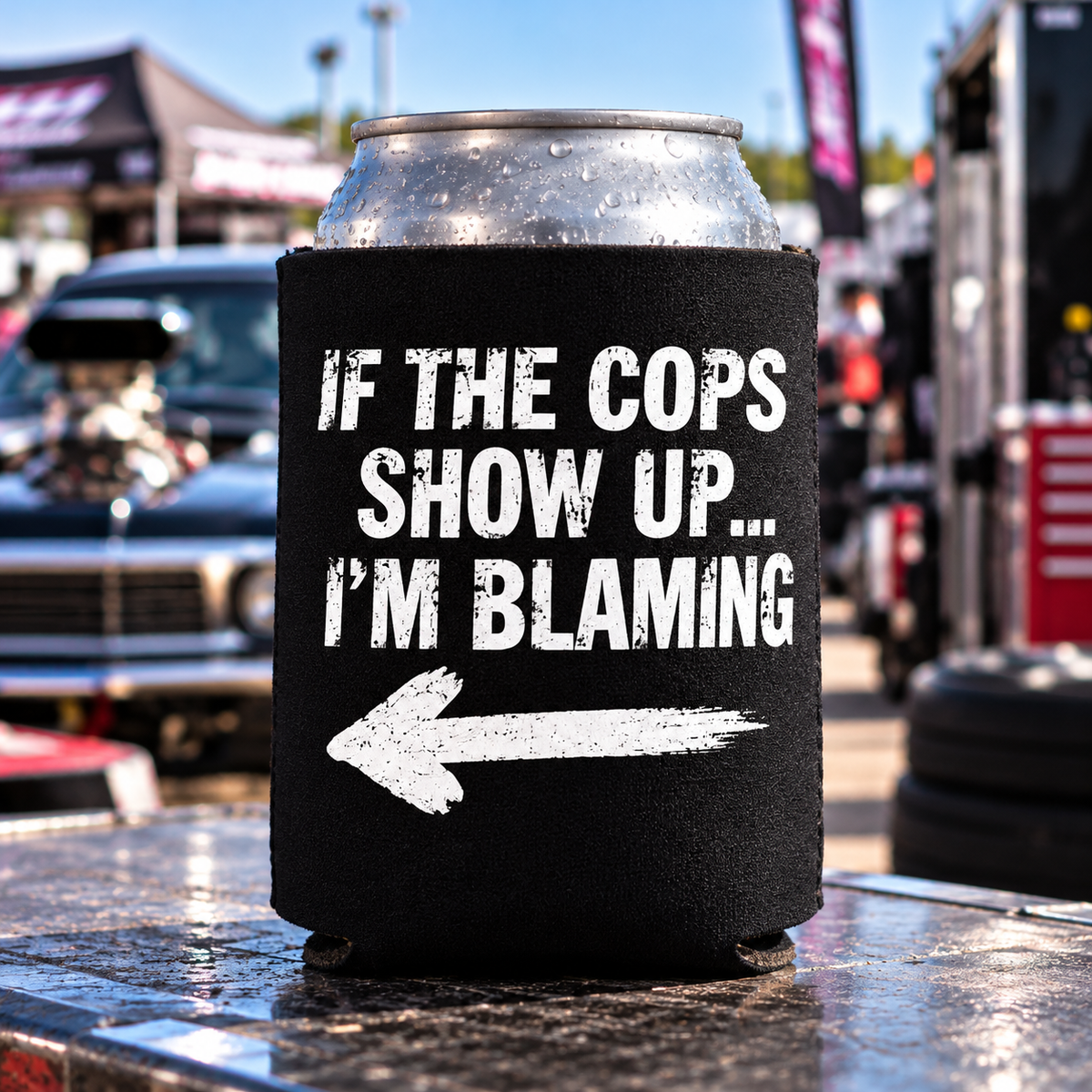 Black Car Chix If The Cops Show Up I'm Blaming foam can koozie with distressed white lettering and left-pointing arrow, displayed at a drag racing event.