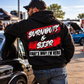 Man wearing black Burnouts & Beer racing hoodie leaning against a classic muscle car at an automotive event