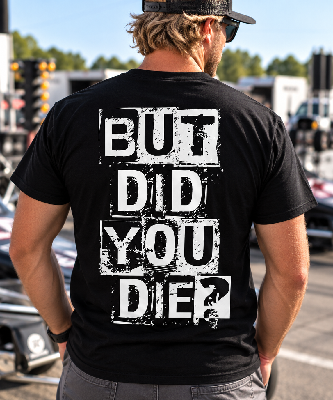 Man wearing black But Did You Die T-shirt with large white distressed back graphic at a drag racing event by Car Chix