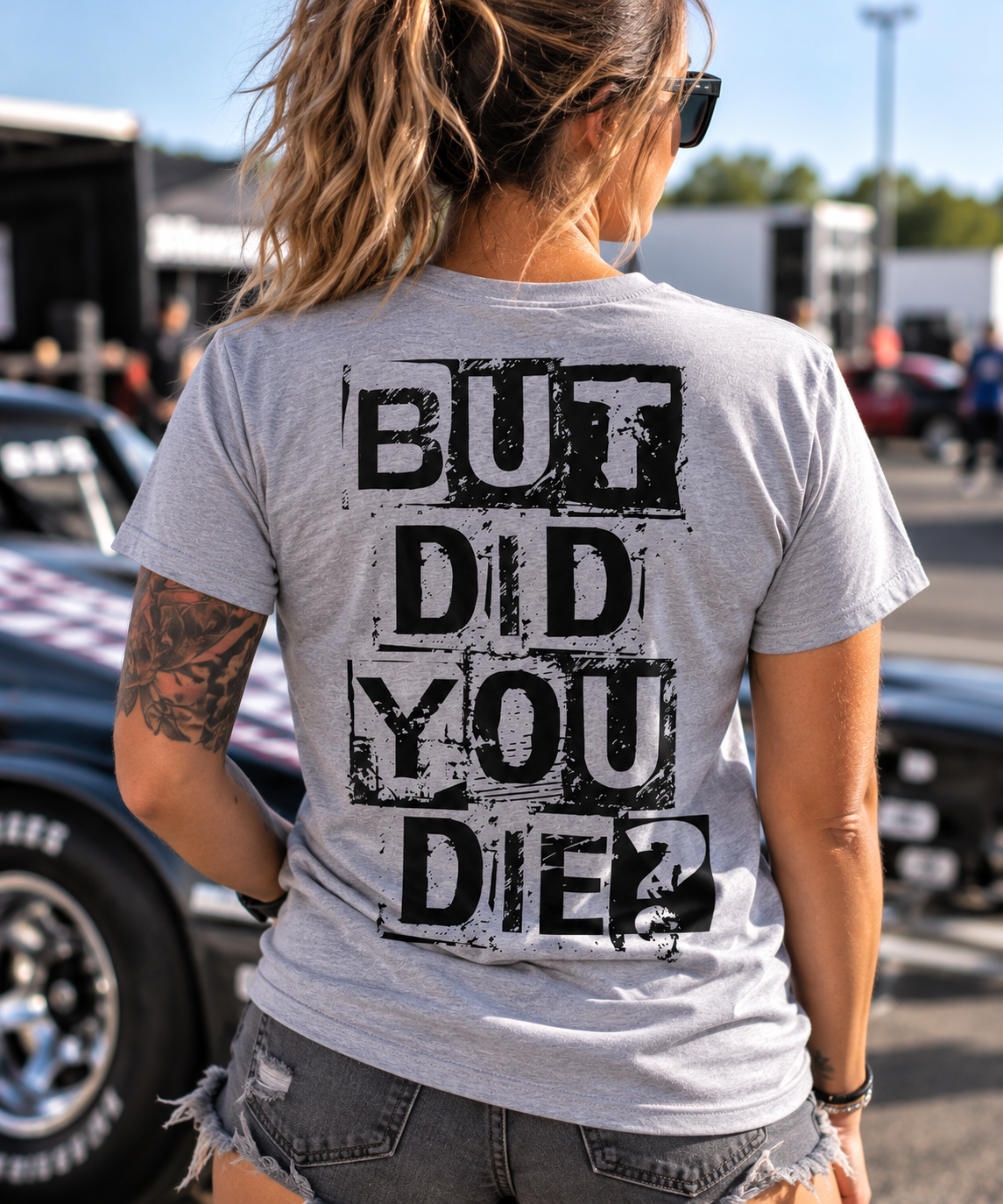 Woman wearing sport gray But Did You Die T-shirt with black distressed back graphic at a motorsports event by Car Chix