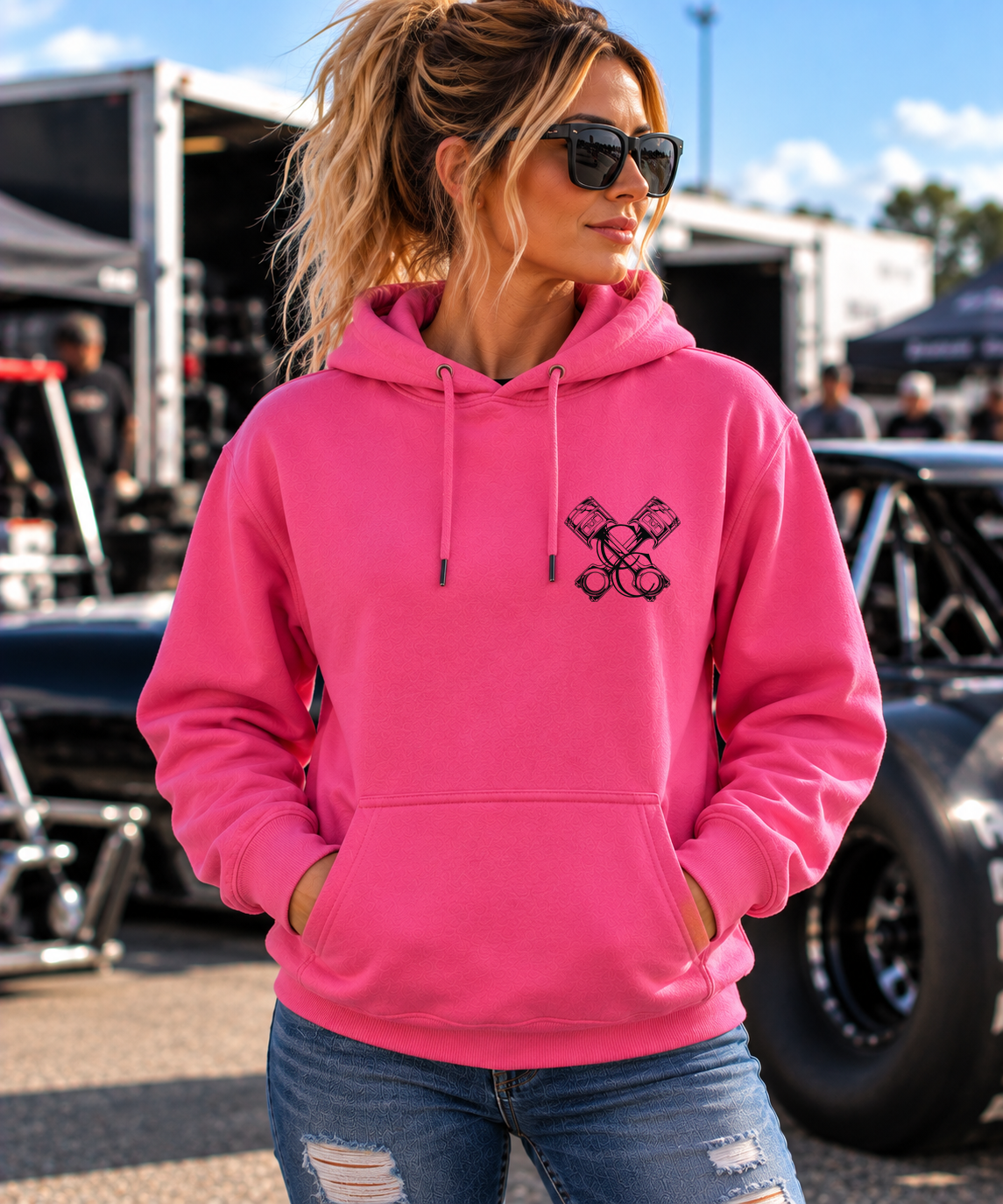Woman modeling pink But Did You Die pullover hoodie, front view at a drag racing event, by Car Chix