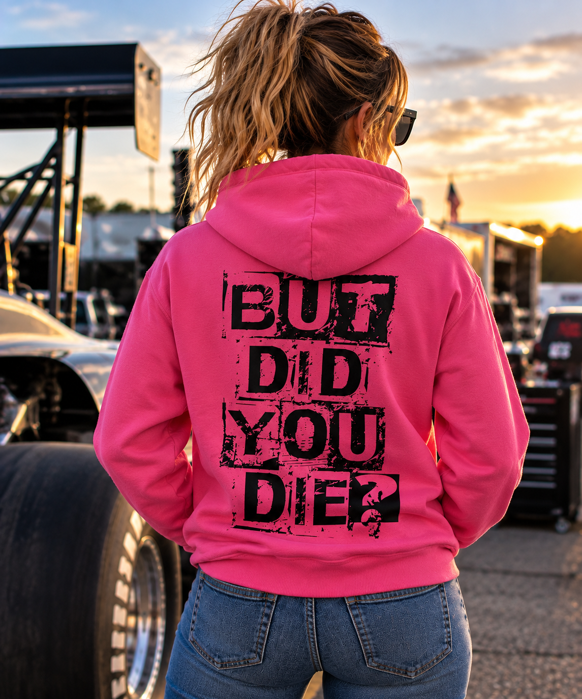 Woman wearing pink But Did You Die hoodie with large black distressed back graphic at a motorsports event by Car Chix