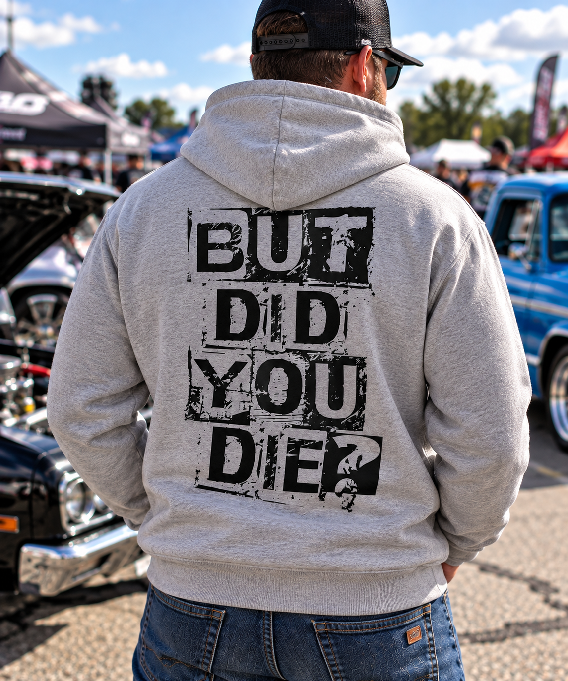 Man wearing grey But Did You Die hoodie with large black distressed back graphic at an outdoor car show by Car Chix