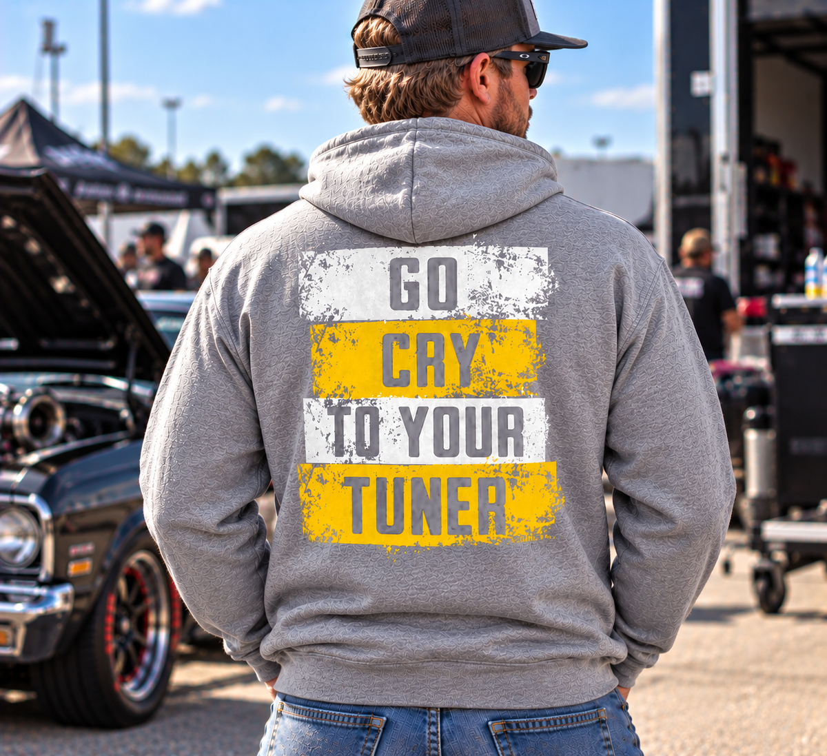 Man wearing a sport grey Car Chix Go Cry to Your Tuner hoodie with distressed white and yellow back graphic and grey knockout lettering at an automotive car meet.