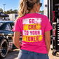 Woman wearing a dark pink Car Chix Go Cry to Your Tuner T-shirt featuring a distressed white and yellow racing design on the back at a drag strip.
