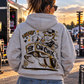 Woman wearing grey Car Chix Haze Memorial Hoodie featuring original Haze and Car Chix drag racing artwork on the back at a racetrack