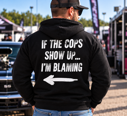 Man wearing black Car Chix If The Cops Show Up I'm Blaming hoodie with distressed white lettering and left-pointing arrow on the back at a drag racing event.