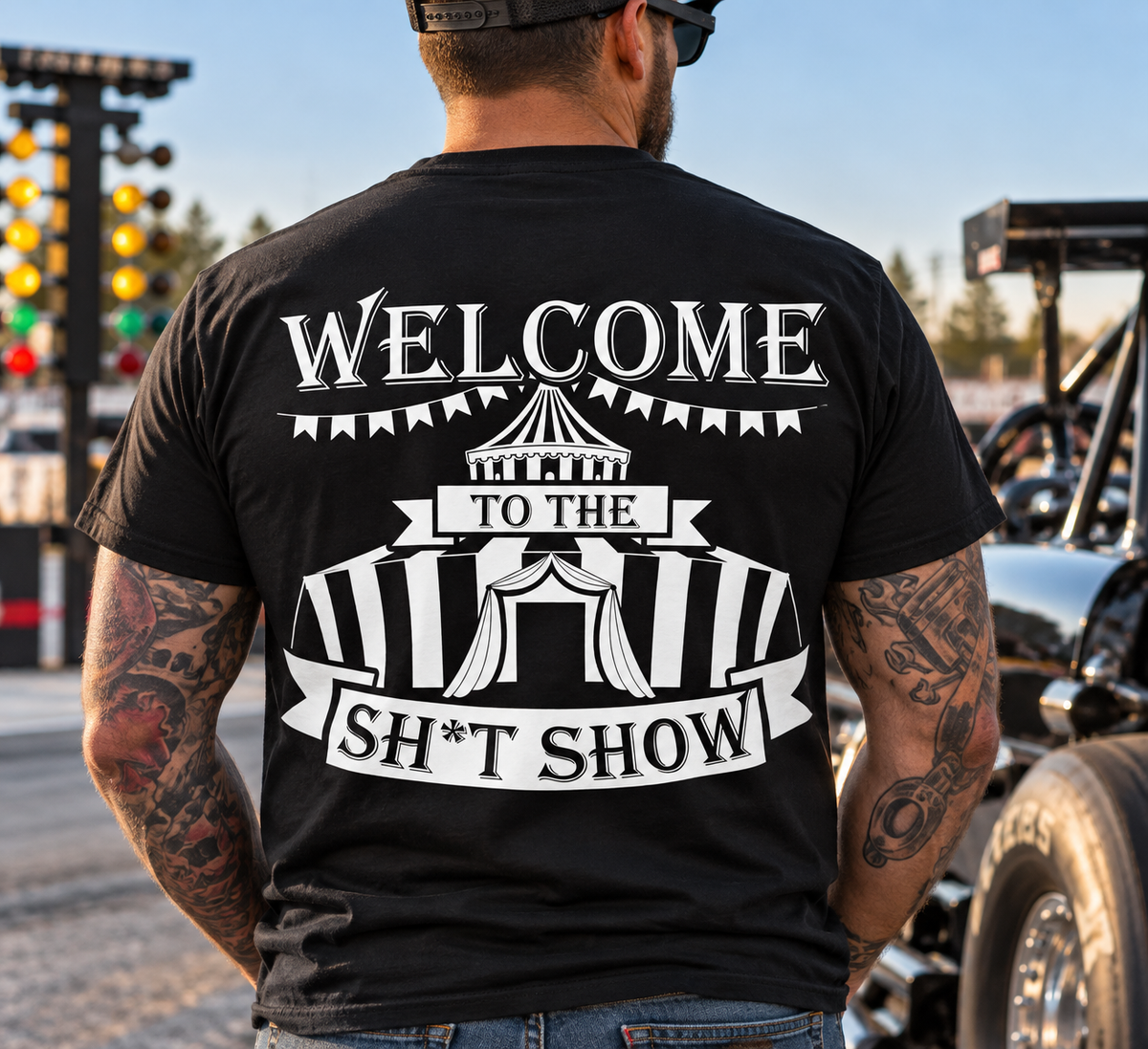 Man wearing black Car Chix Welcome to the Sh*tshow T-shirt with large white circus graphic on the back at a drag racing event