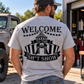 Man wearing grey Car Chix Welcome to the Sh*tshow T-shirt featuring black circus tent artwork on the back outside an automotive garage