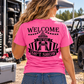 Woman wearing pink Car Chix Welcome to the Sh*tshow T-shirt with black carnival graphic on the back at an off-road racing event