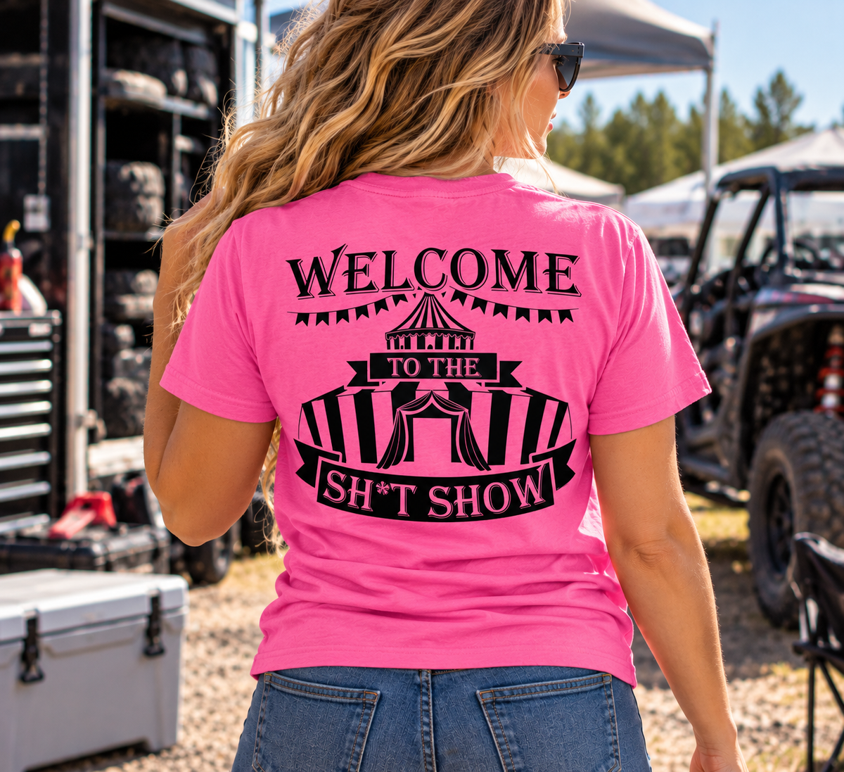 Woman wearing pink Car Chix Welcome to the Sh*tshow T-shirt with black carnival graphic on the back at an off-road racing event