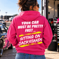 Woman wearing a dark pink Car Chix Your Car Must Be Pretty Fast Sitting on Jackstands hoodie with bold white lettering and neon yellow racing-inspired accents in a motorsports pit area.
