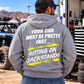 Man wearing a sport grey Car Chix Your Car Must Be Pretty Fast Sitting on Jackstands hoodie featuring white distressed text and neon yellow brushstroke graphics at an off-road motorsports event.