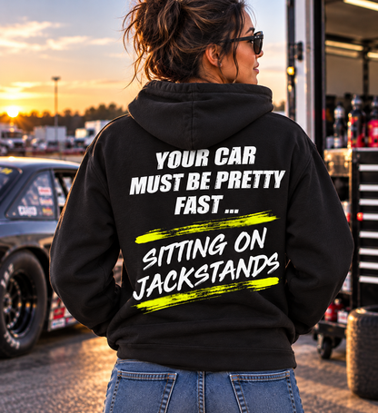 Woman wearing a black Car Chix Your Car Must Be Pretty Fast Sitting on Jackstands hoodie with distressed white lettering and neon yellow accents at a drag racing track.