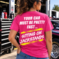 Woman wearing a dark pink Car Chix Your Car Must Be Pretty Fast Sitting on Jackstands T-shirt with white lettering and neon yellow brushstroke accents at a racetrack.