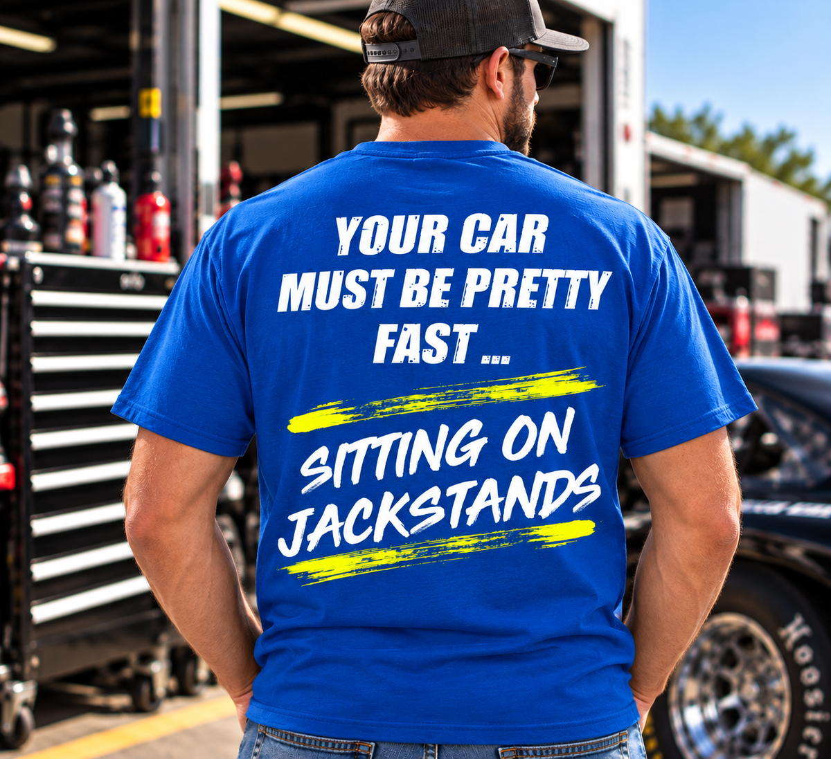 Man modeling a royal blue Car Chix Your Car Must Be Pretty Fast Sitting on Jackstands T-shirt with white distressed text and neon yellow racing-inspired graphics.