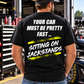 Man wearing a black Car Chix Your Car Must Be Pretty Fast Sitting on Jackstands T-shirt with white distressed lettering and neon yellow accents in a racing garage.