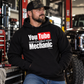Man wearing black YouTube Certified Mechanic hoodie in an automotive garage with lifted truck and tools by Car Chix