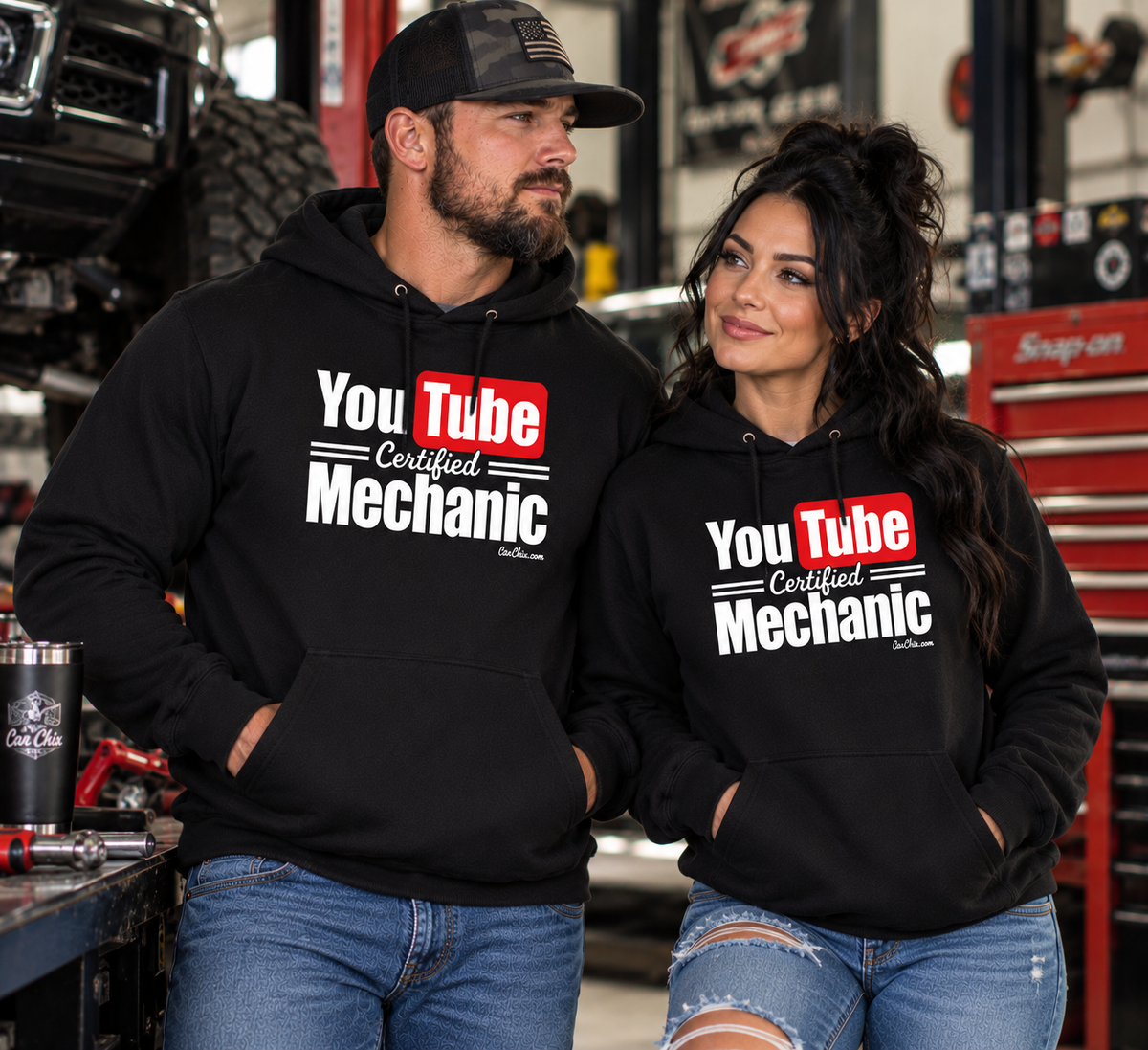 Man and woman wearing black YouTube Certified Mechanic hoodies together in an automotive garage by Car Chix