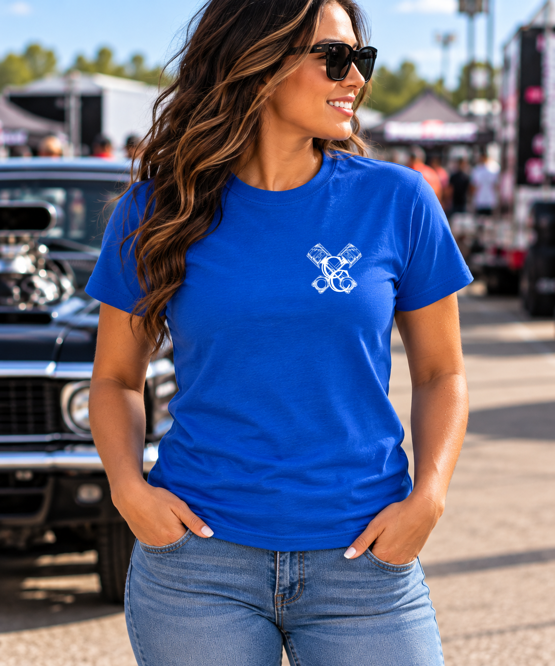 Woman wearing blue Car Chix unisex T-shirt shown from the front at a car show, featuring a plain chest area for the Car Chix Piston logo.