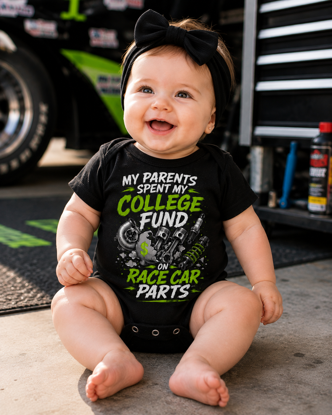 Baby wearing College Fund Race Car Parts infant racing bodysuit in a motorsports garage