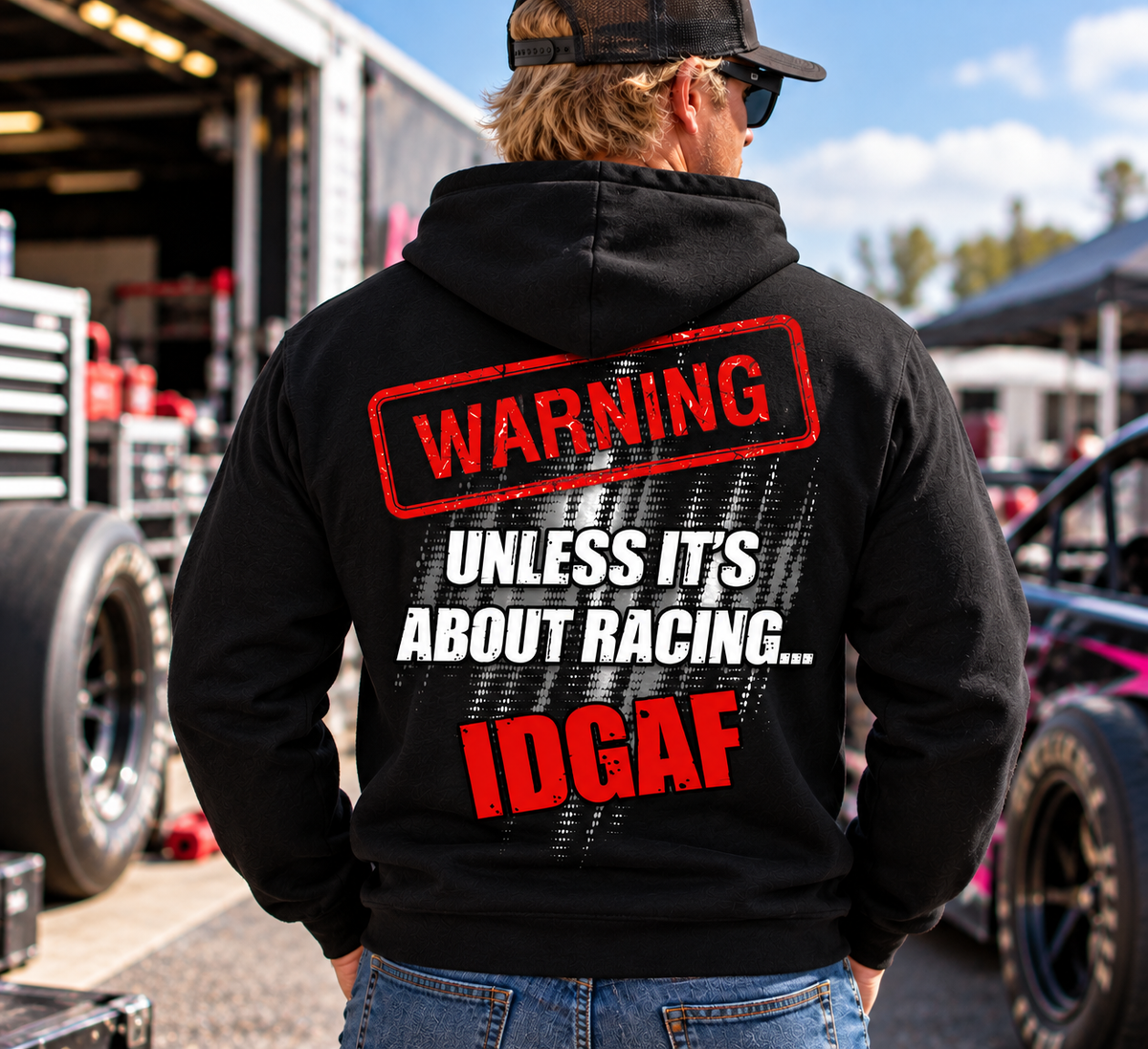 Man wearing black Car Chix Unless It's About Racing IDGAF hoodie featuring large red and white warning graphic on the back at a motorsports racing event.