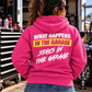 Woman wearing a dark pink Car Chix What Happens in the Garage Stays in the Garage hoodie featuring white brushstroke lettering and a neon yellow back graphic at an automotive racing garage.