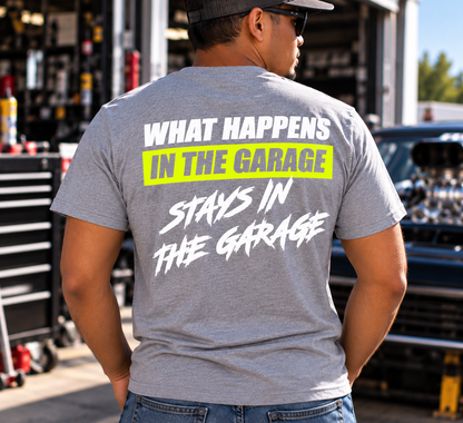 Man wearing a grey Car Chix What Happens in the Garage Stays in the Garage T-shirt with white lettering and neon yellow back graphic in a racing workshop.